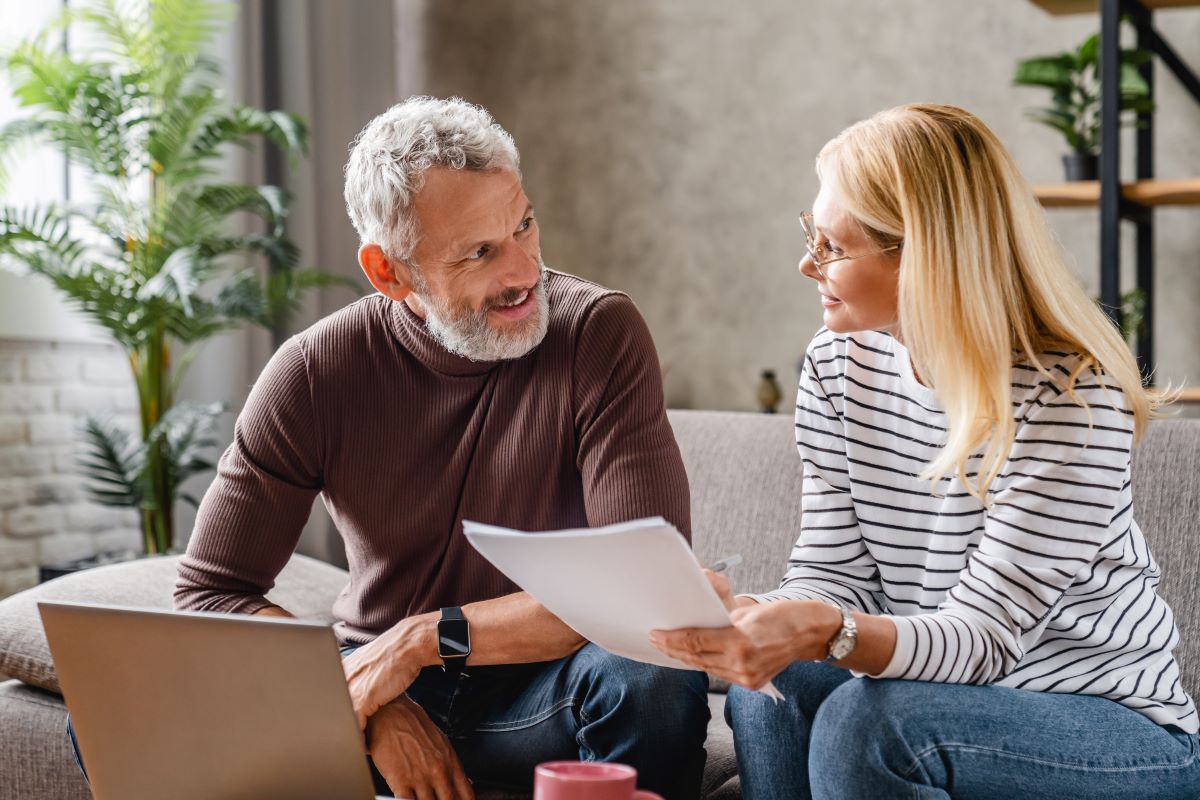 Smiling middle aged couple with laptop studying documents