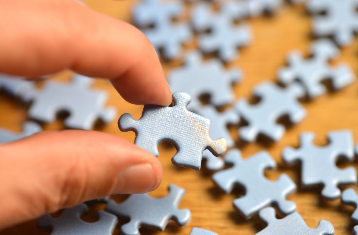 Jigsaw puzzle piece hold by someone's fingers